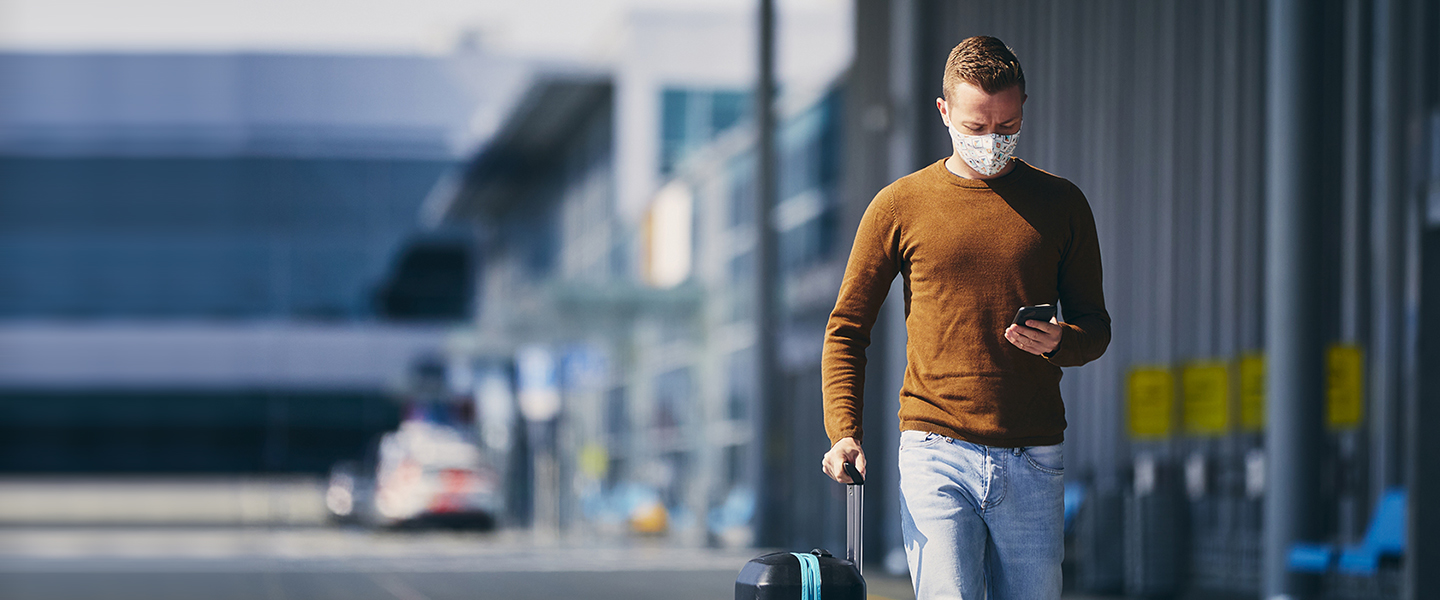 passenger at airport walking outside terminal with a mask on